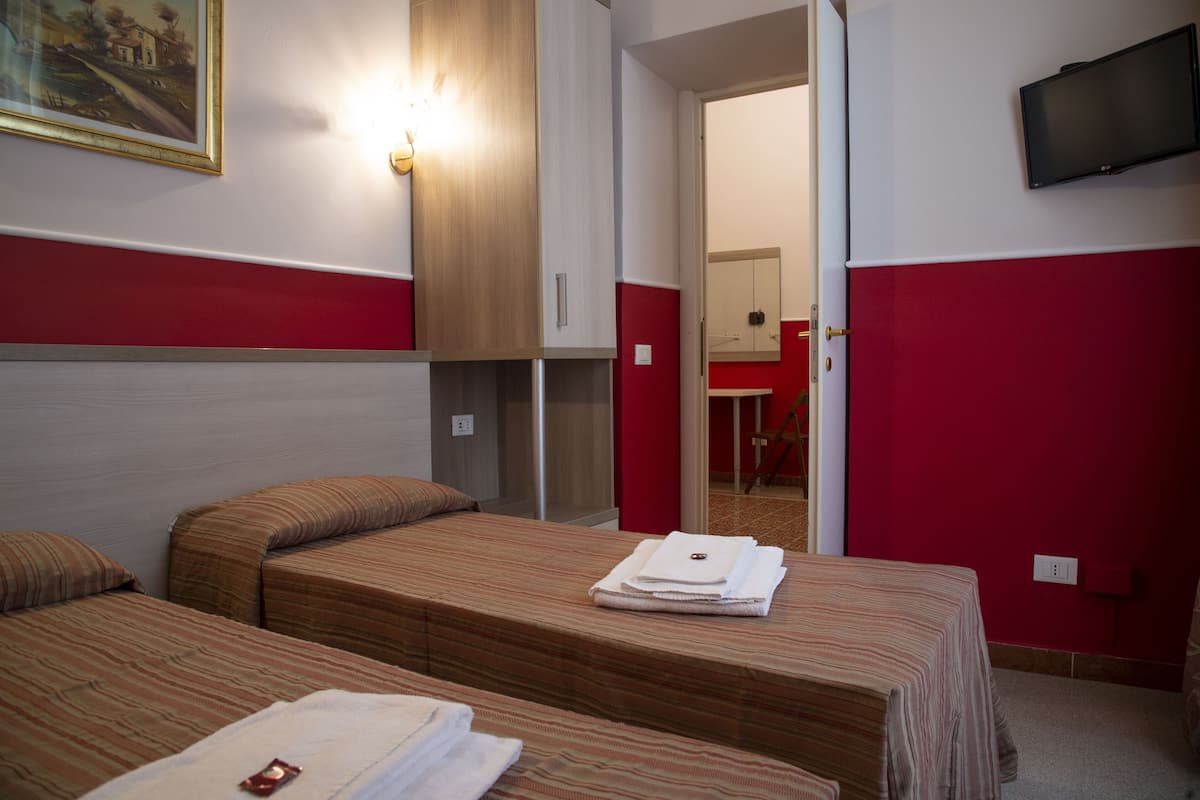 A hotel room with two beds, a TV mounted on the wall, and a painting on the wall.