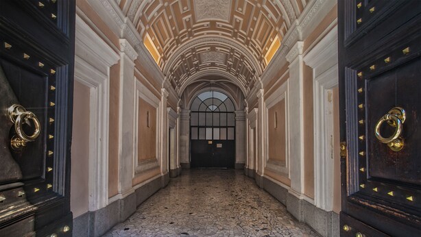 A hallway with a tiled floor, arched ceiling, and dark wooden doors with gold accents. - Domus Napoleone (Rome)