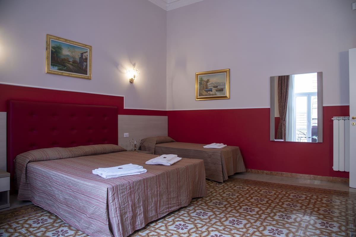 A hotel room with two beds, a red headboard, patterned floor, and two framed pictures on the walls.