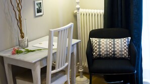 Une pièce avec une table blanche, une chaise noire dotée d’un coussin à motifs, une lampe blanche et un radiateur.