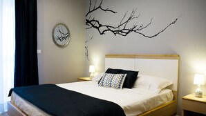 Un lit bien fait, avec une couette noire et blanche, deux lampes de chevet, une horloge murale et une œuvre d’art représentant une branche accrochée au mur.