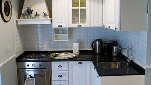 Une cuisine avec des meubles blancs, un plan de travail noir, une cuisinière, un évier et un luminaire suspendu.