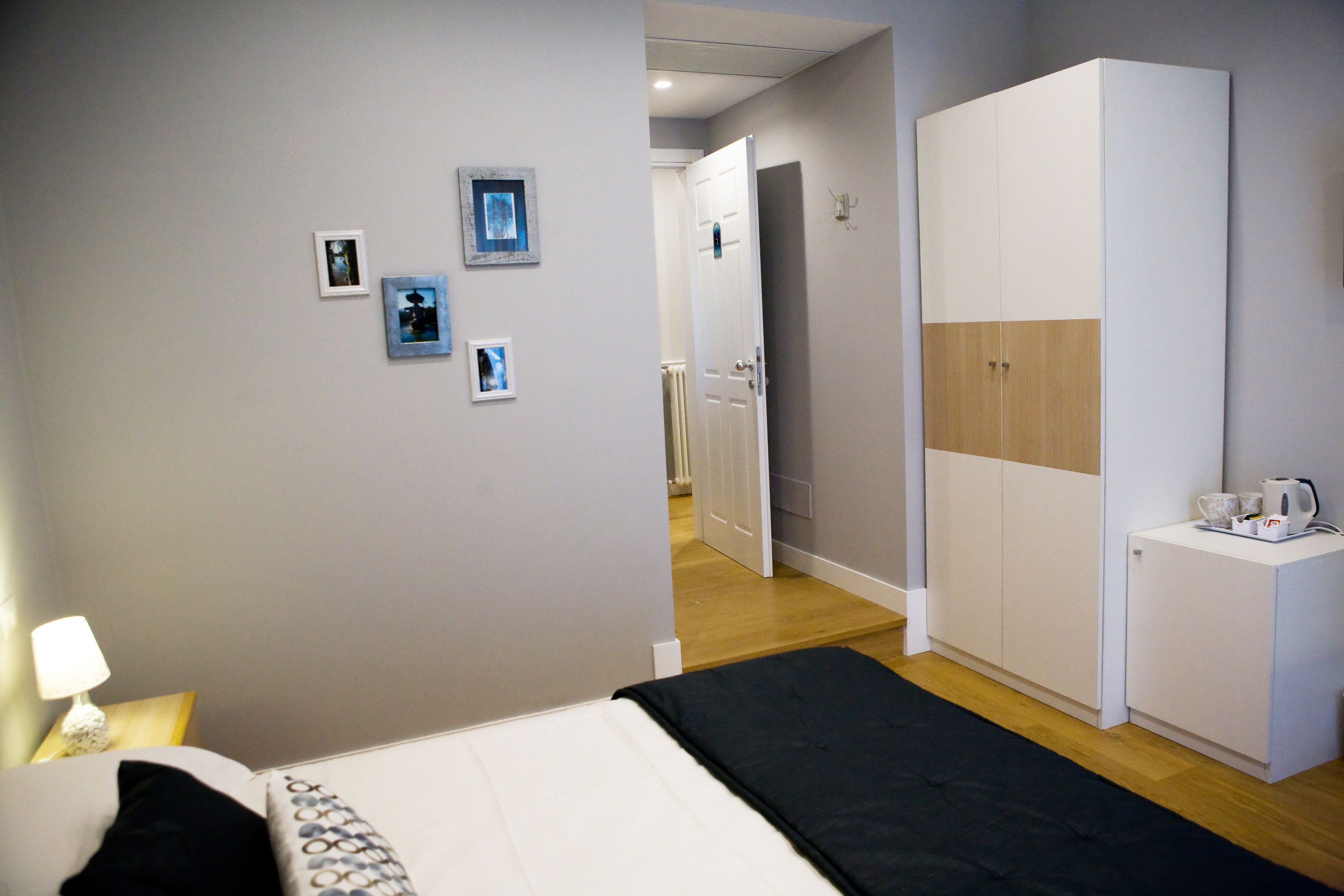 A bedroom with a bed, a wardrobe, and a desk with a kettle.
