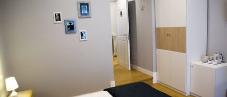 A bedroom with a bed, a wardrobe, and a desk with a kettle.