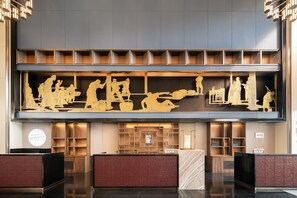Uma área de recepção de hotel com design moderno, incluindo um balcão de recepção, espaço para sentar e um grande painel decorativo.