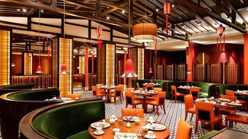 A restaurant with round tables, green upholstered booths, and orange chairs.