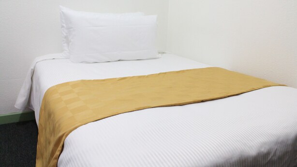A single bed with a white pillow and a mustard-colored blanket. - Union Hotel (San Francisco)