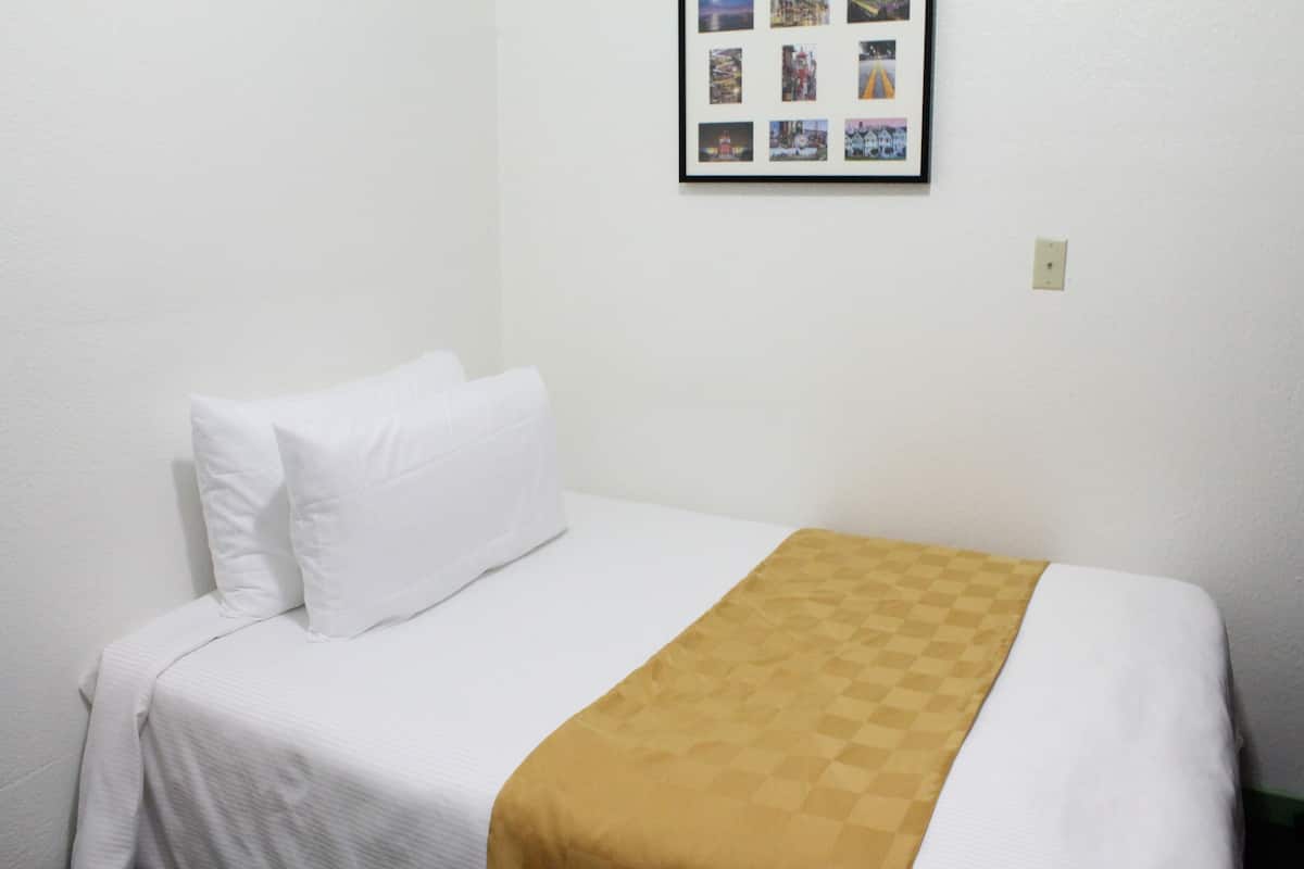 A single bed with white bedding and a brown blanket, a framed photo collage on the wall, and a light switch.