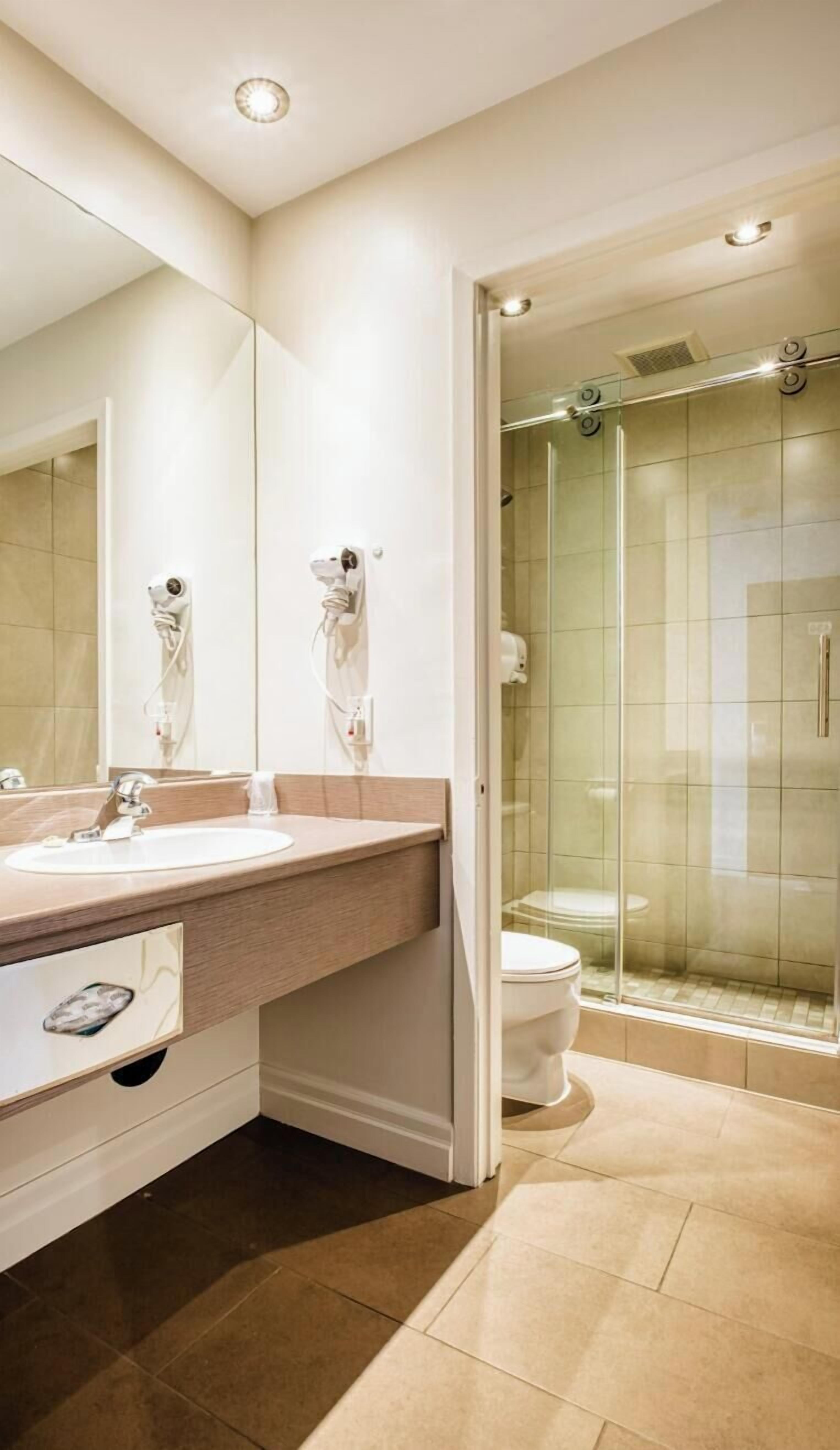A modern bathroom with a large mirror, a sink, a toilet, and a glass-enclosed shower.