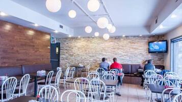 Interior de restaurante con mesas altas, sillas blancas, pared de piedra y televisor de pantalla plana montado en la pared.