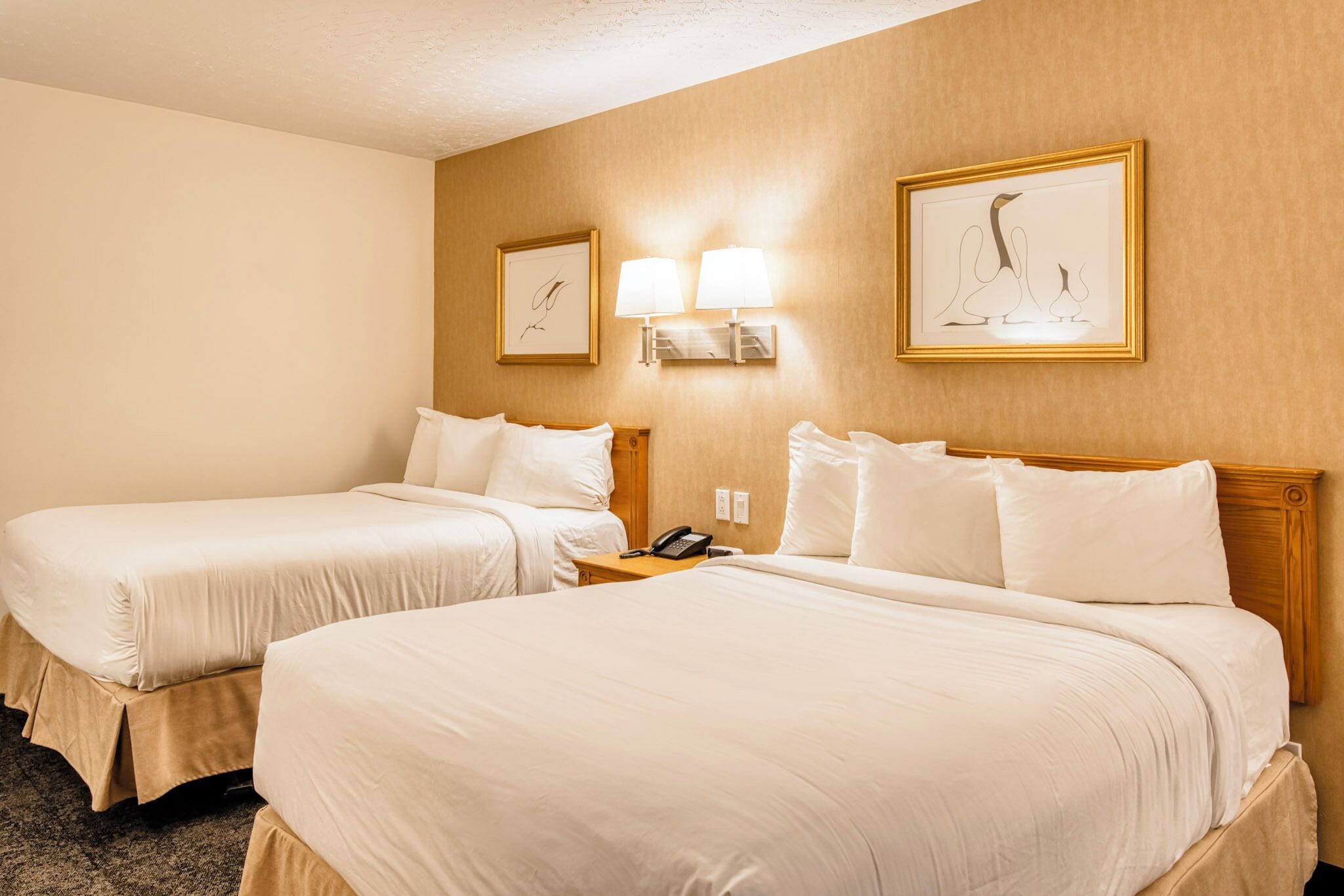 A hotel room with two beds, a nightstand with a phone, and wall-mounted lamps.