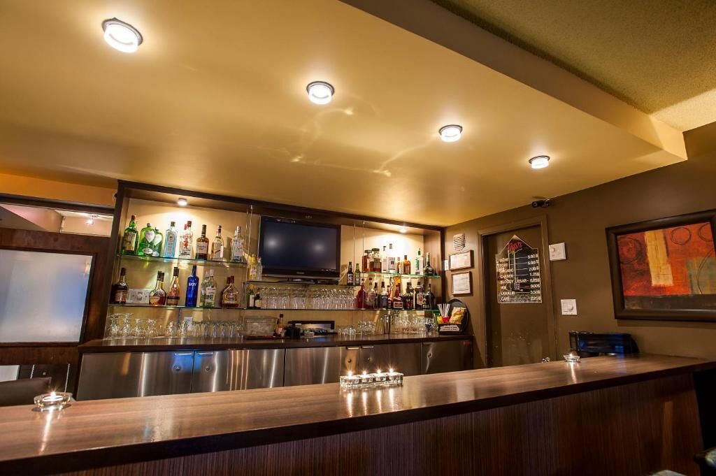 A bar area with a counter, shelves of bottles, glasses, and a television.