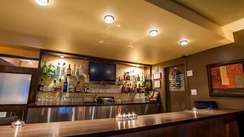 A bar area with a counter, shelves of bottles, glasses, and a television.