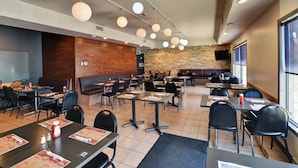 Un restaurant avec des banquettes et des tables, un mur en pierre et un téléviseur fixé au mur.