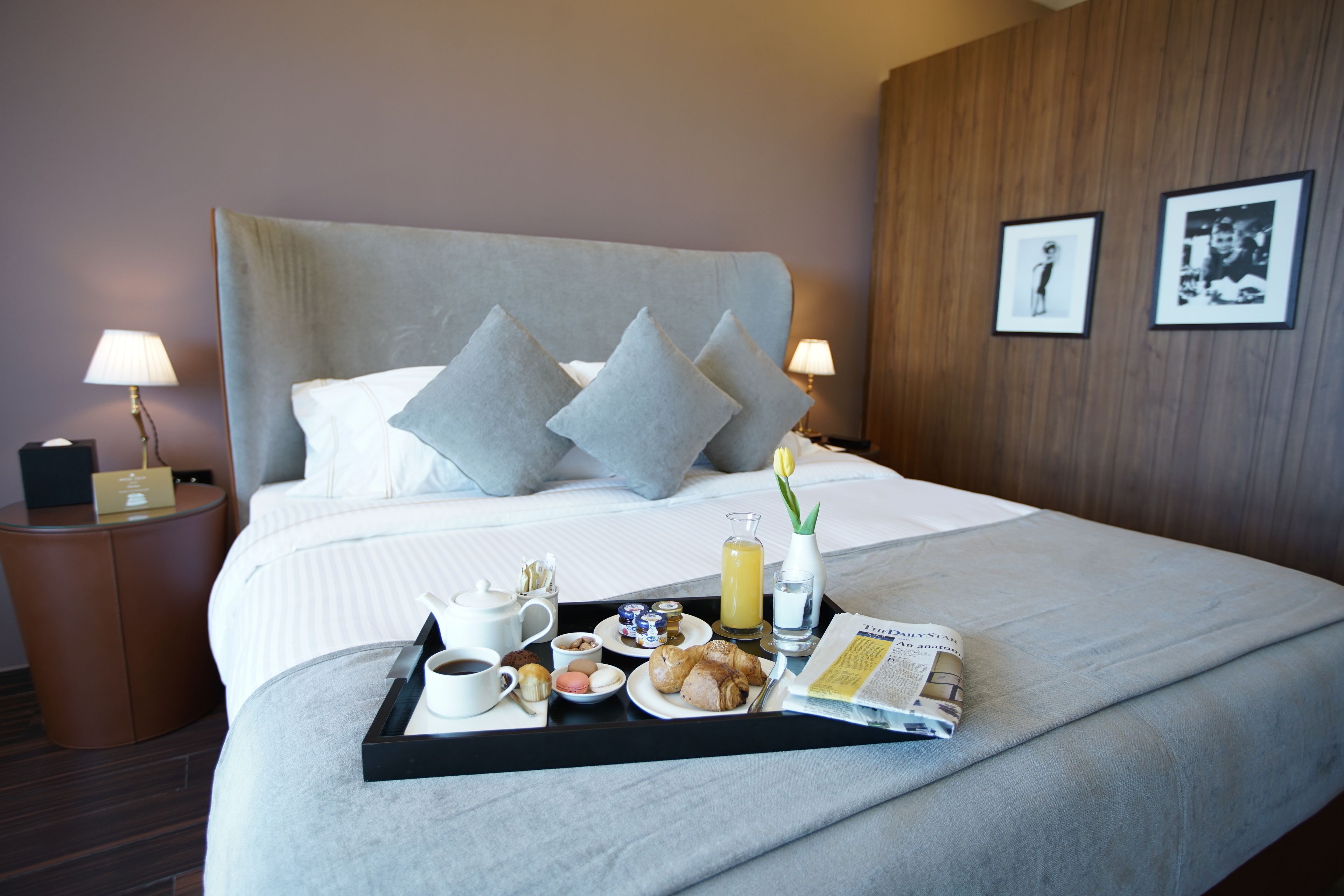 A hotel room with a large bed, a tray with breakfast items, and a magazine on the bed.