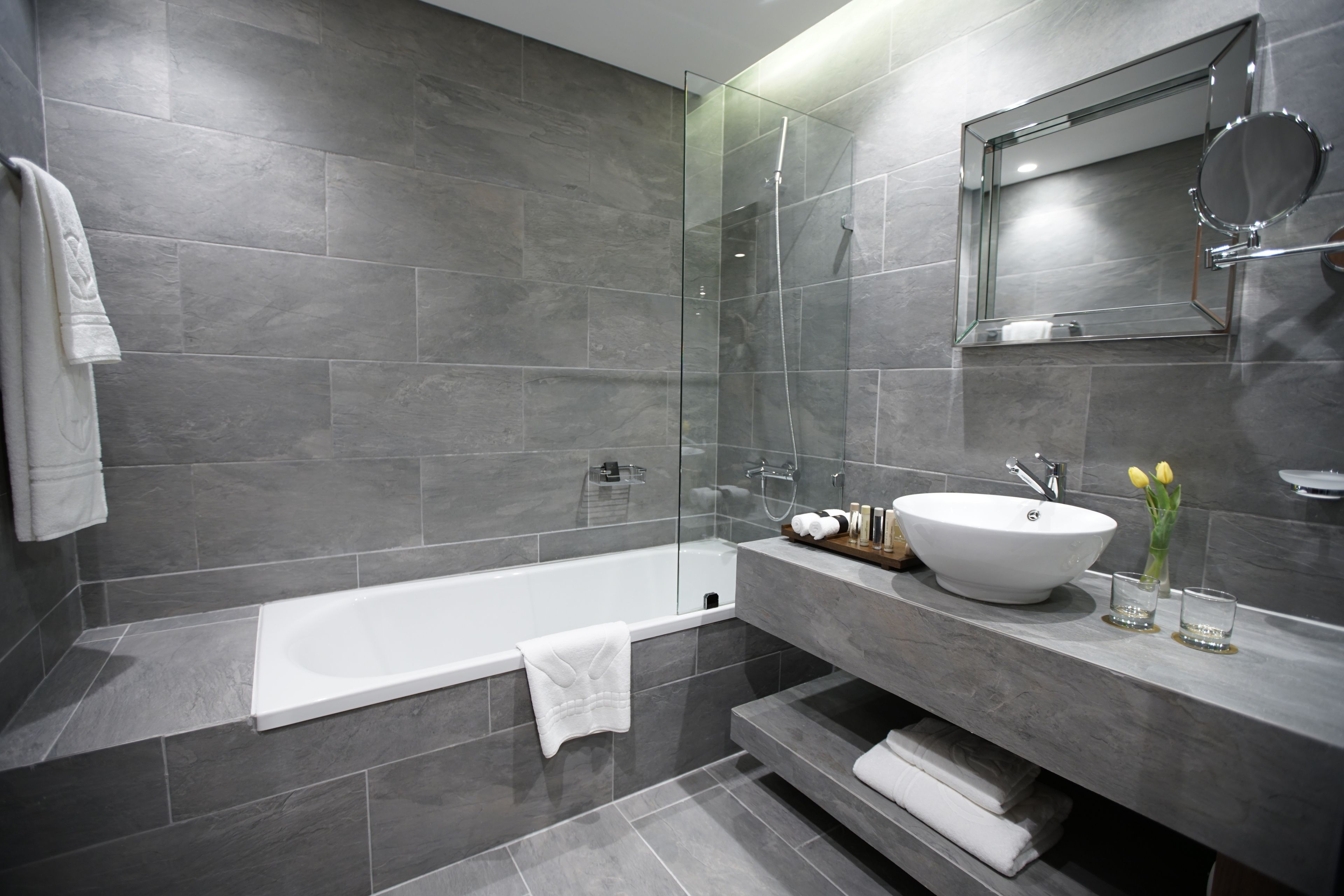 A modern bathroom with a glass-enclosed shower, a white bathtub, and a marble vanity with a sink and mirror.