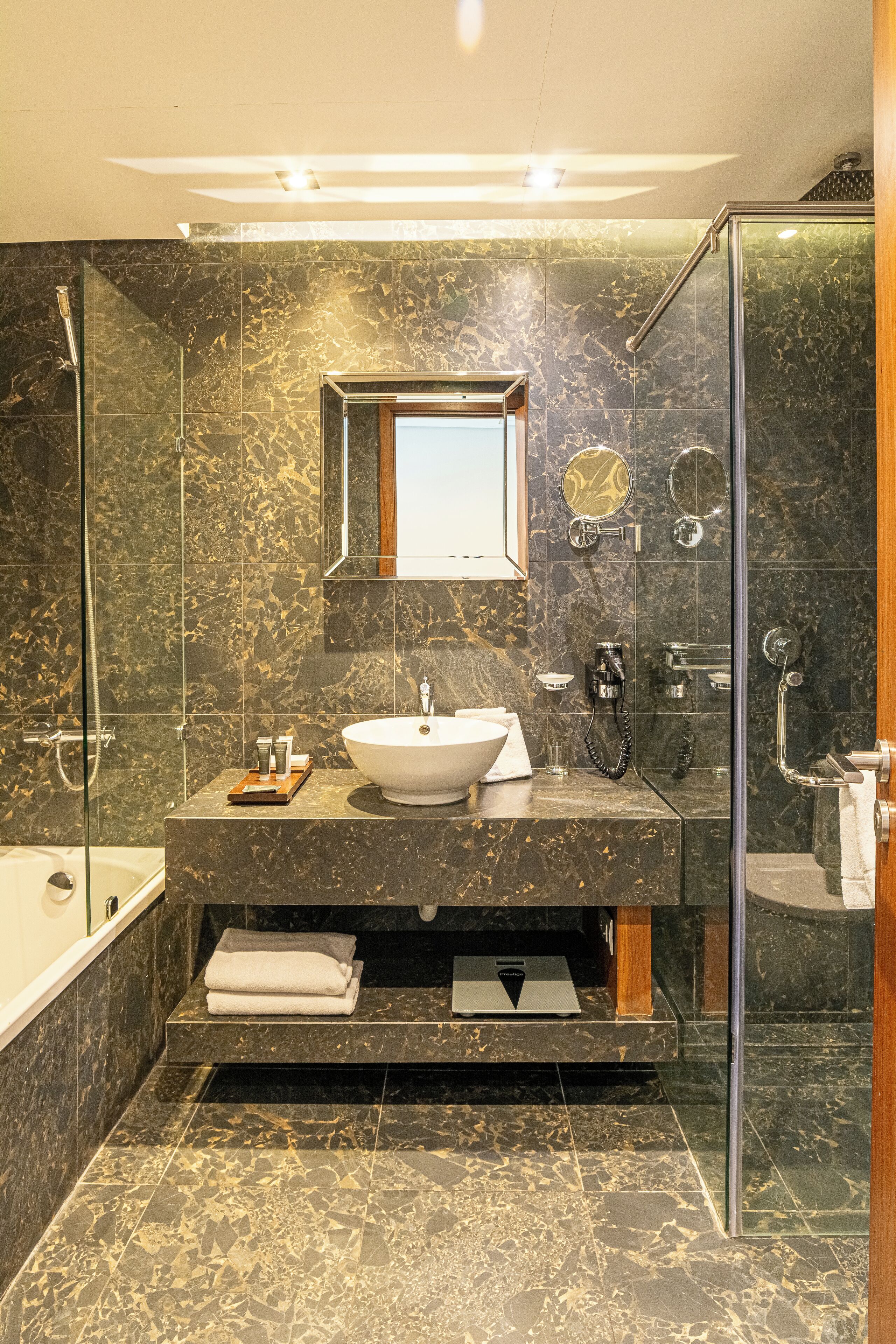 A modern bathroom with a marble sink, a glass shower enclosure, and a vanity with a mirror.