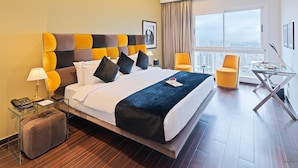 A modern hotel room with a large bed, a glass table, and a view of the city. - Royal Tulip Achrafieh (Beirut)