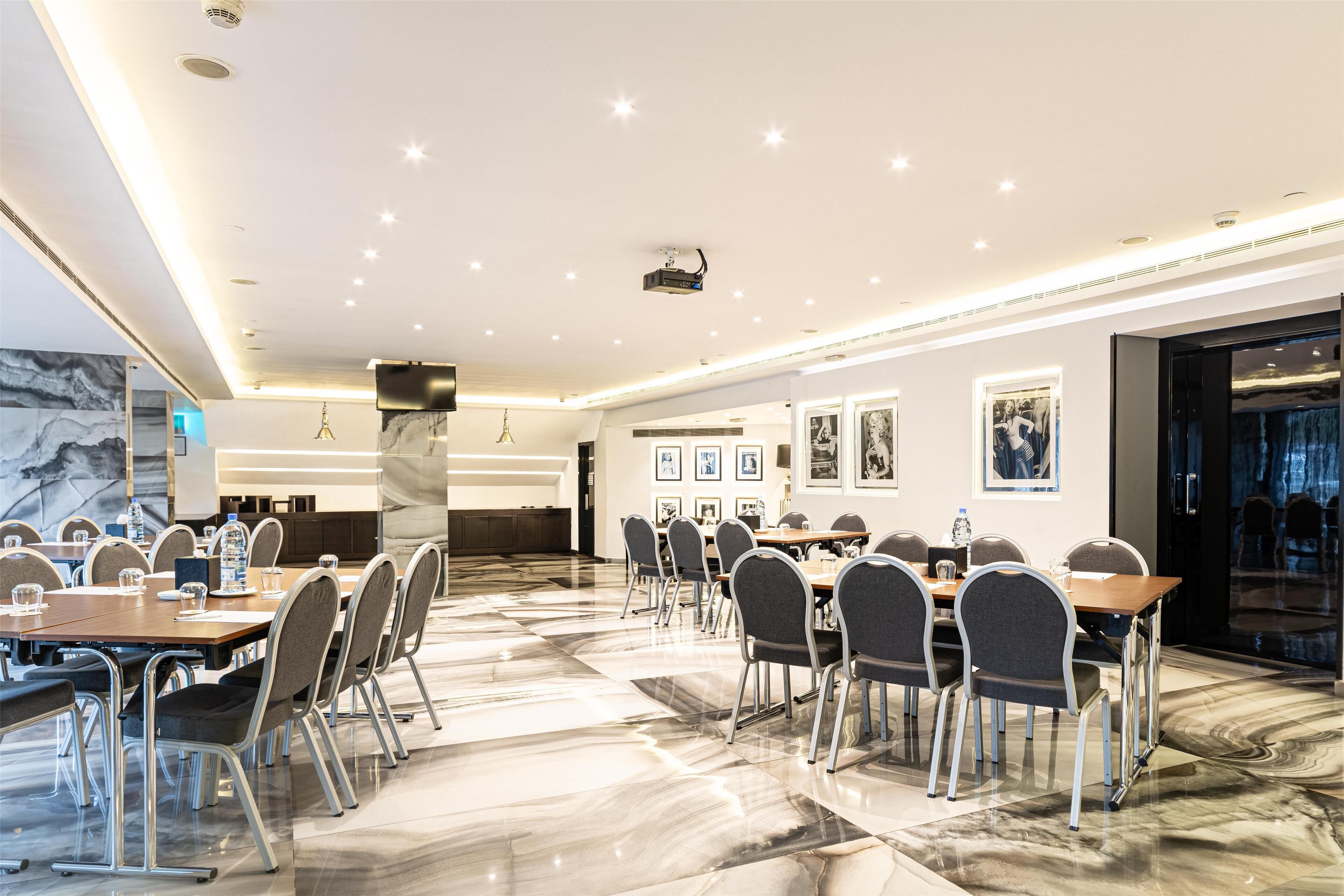 A modern conference room with marble flooring, multiple tables, and chairs, equipped with a projector and framed pictures on the walls.