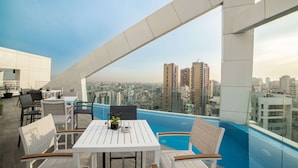 A rooftop terrace with tables and chairs, a pool, and a city view. - Royal Tulip Achrafieh (Beirut)