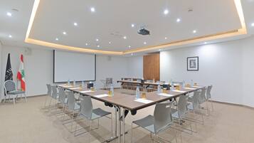 A conference room with a long table, chairs, flags, a projector, and a screen.