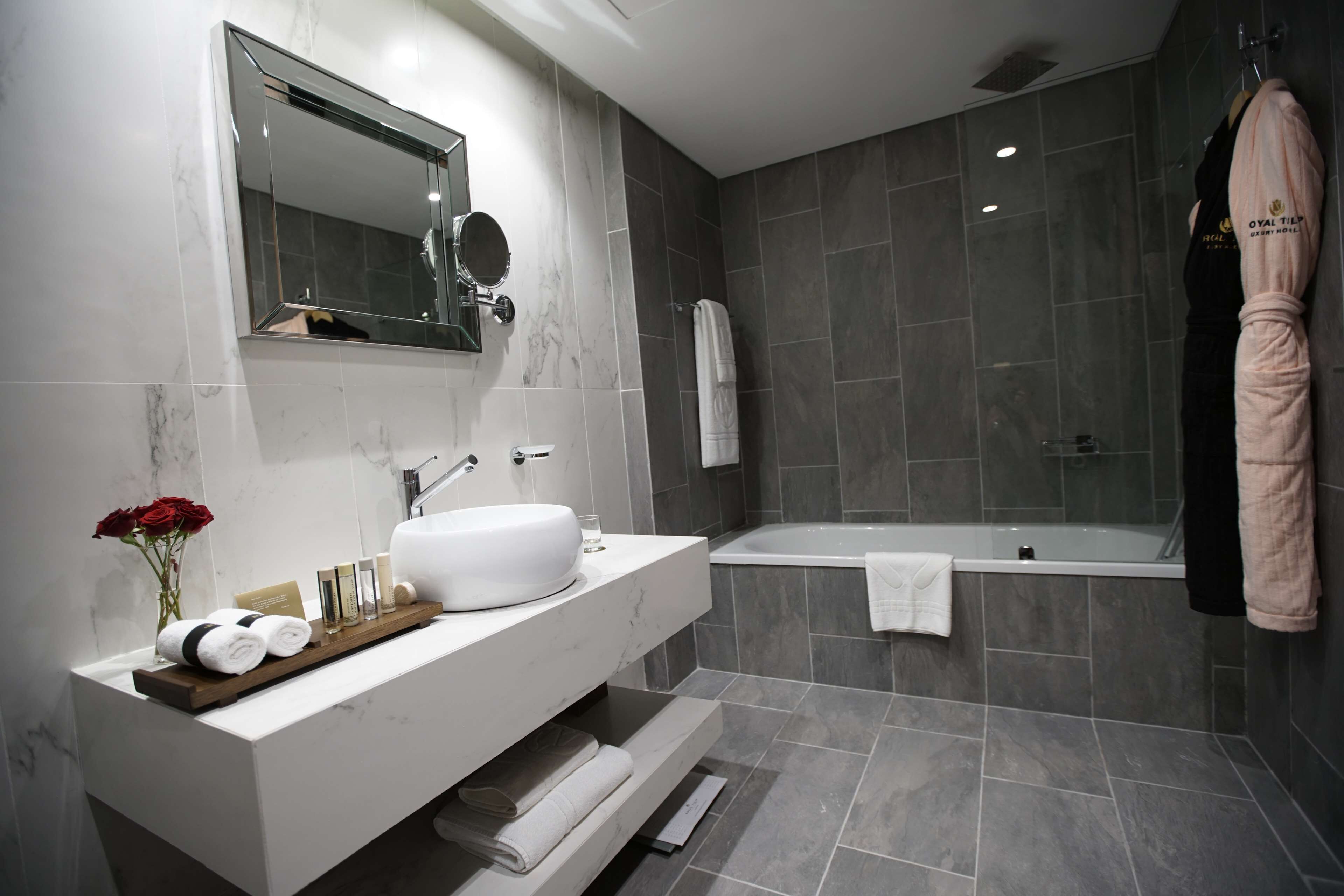 A modern bathroom with a marble vanity, a large mirror, a bathtub, and a towel rack.