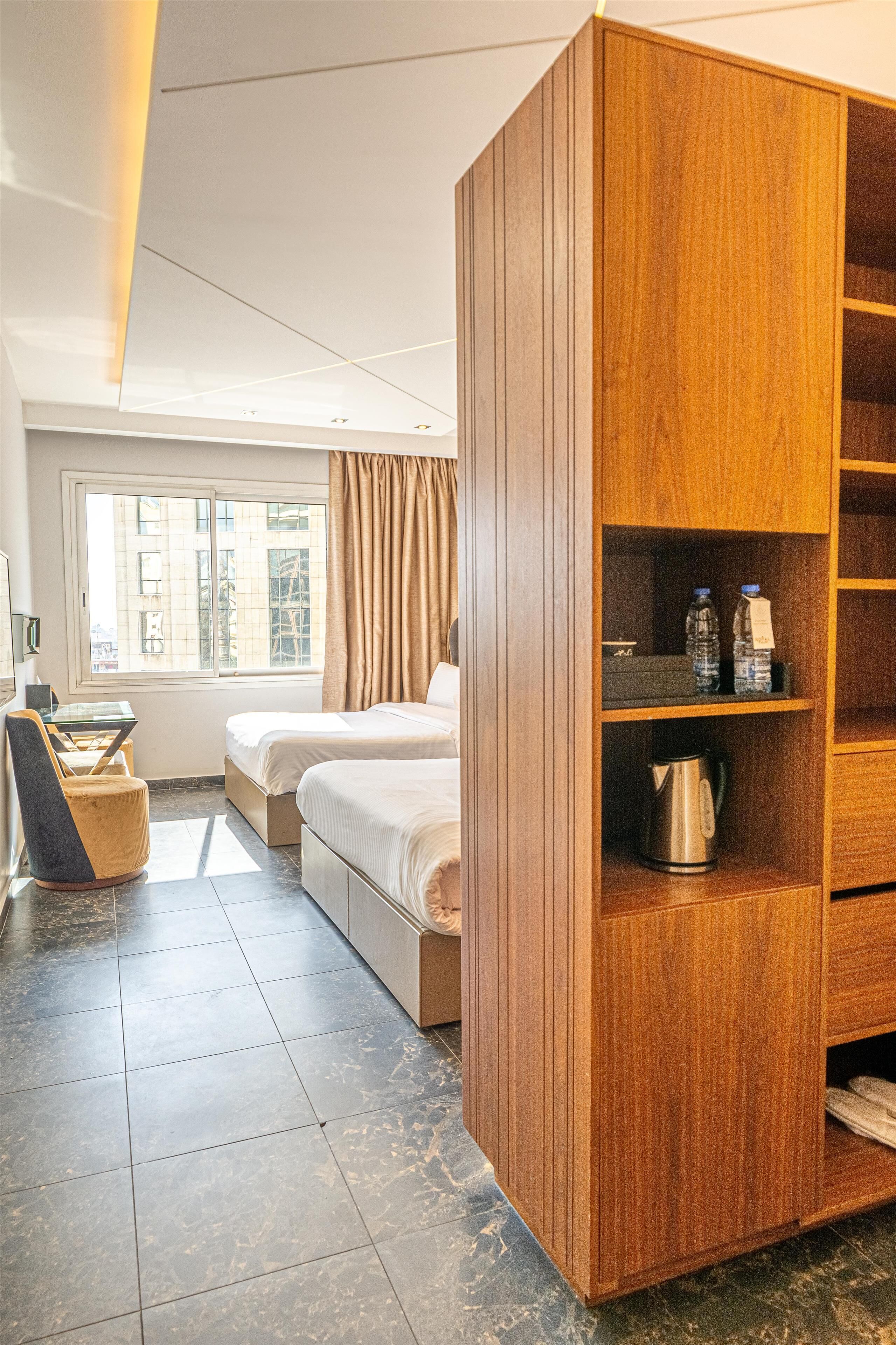 Habitación de hotel con dos camas, un armario de madera, una cafetera y un escritorio con una silla.