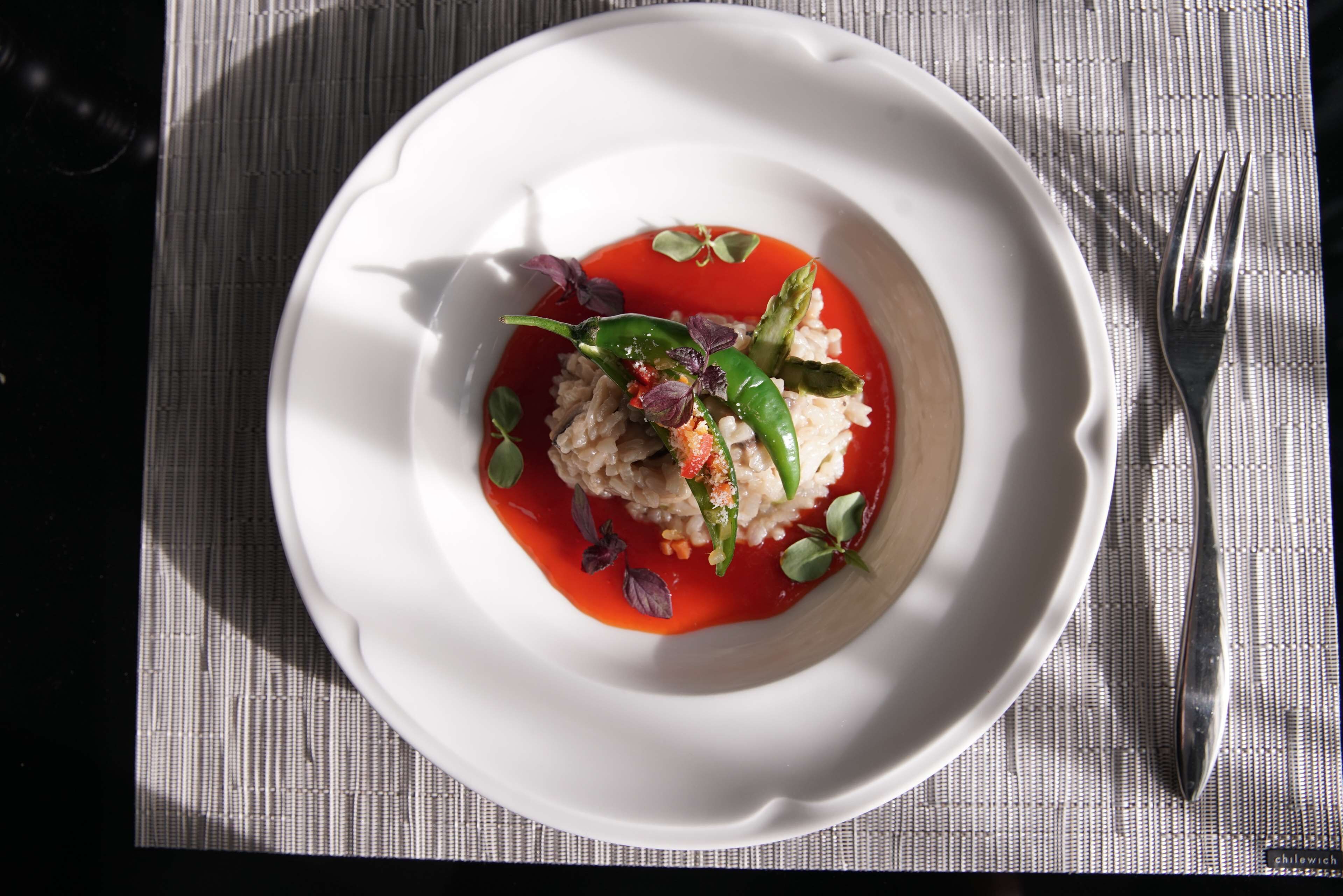 A white plate with a dish of rice and vegetables, garnished with red sauce and herbs, on a textured placemat.