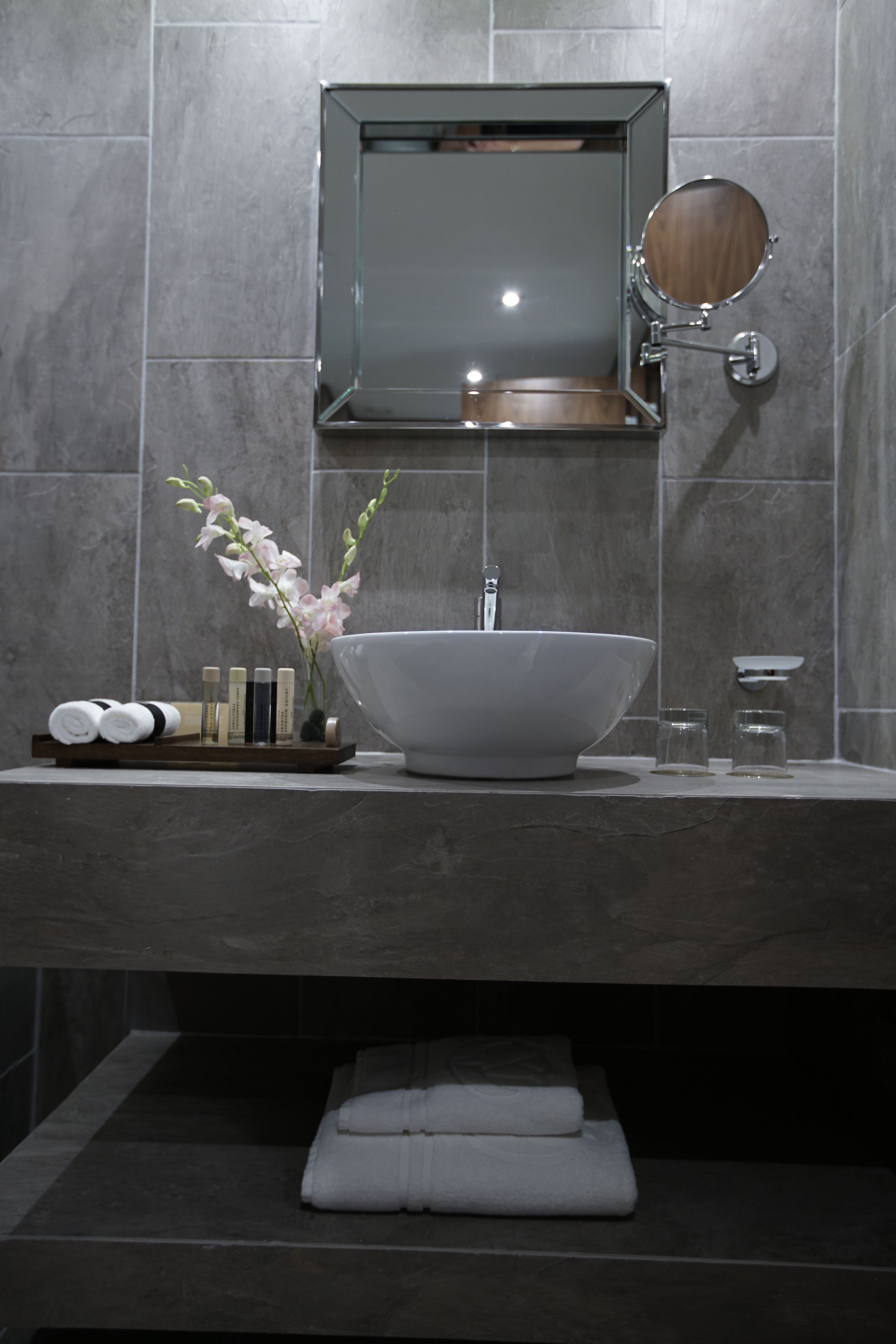 A modern bathroom with a large white sink, a mirror, and a small vase with flowers.