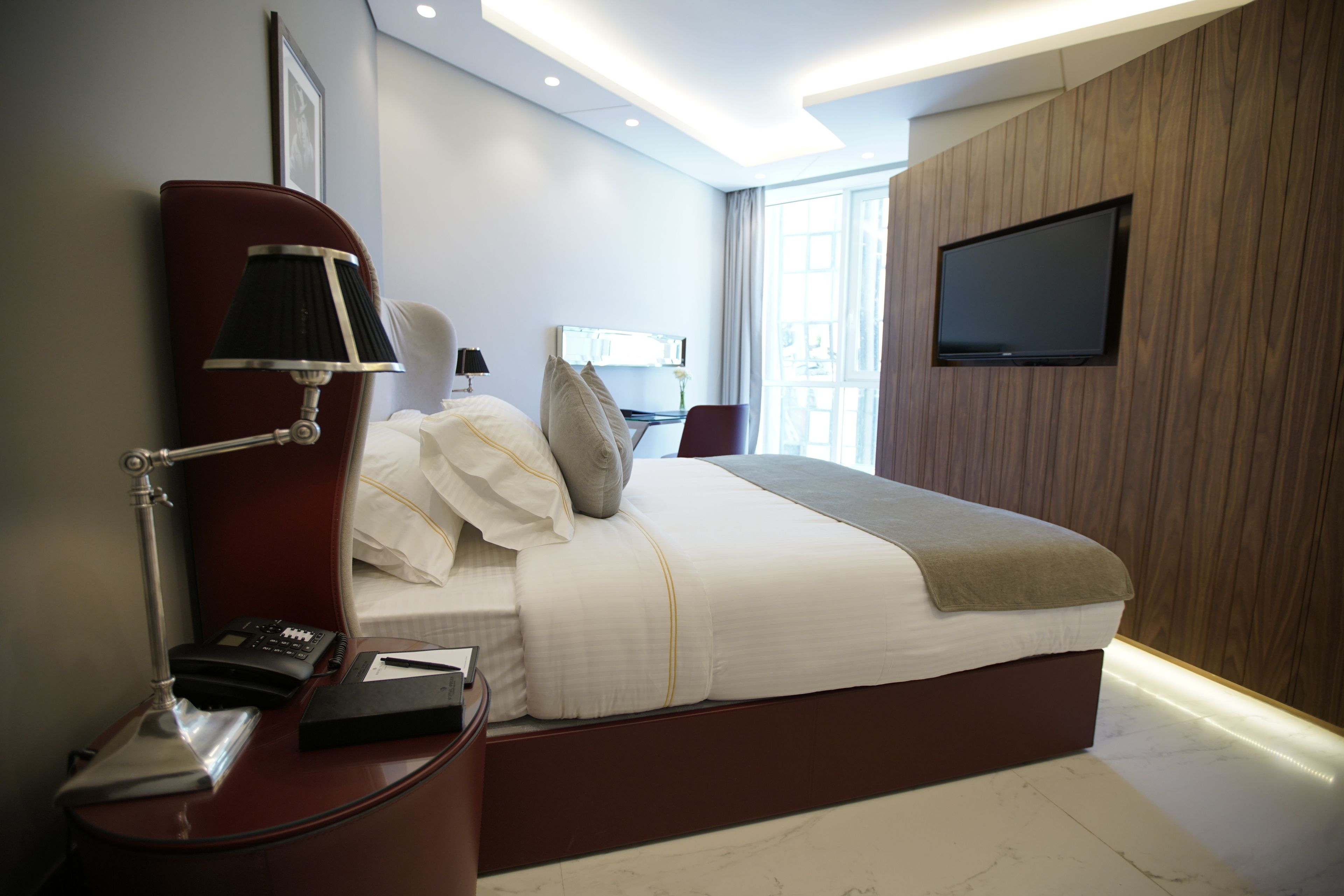 Een moderne hotelkamer met een groot bed, nachtkastje met lamp, een flatscreen televisie aan de muur en een raam met uitzicht op de stad.