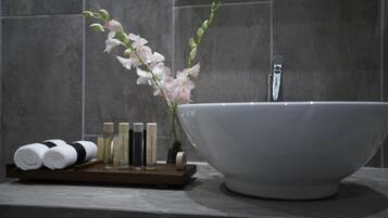 Un baño con un lavamanos grande de color blanco, una bandeja de madera con artículos de aseo y una orquídea rosa.