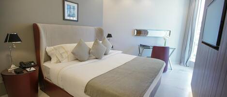 A modern hotel room with a large bed, bedside lamps, a small table, and a TV.