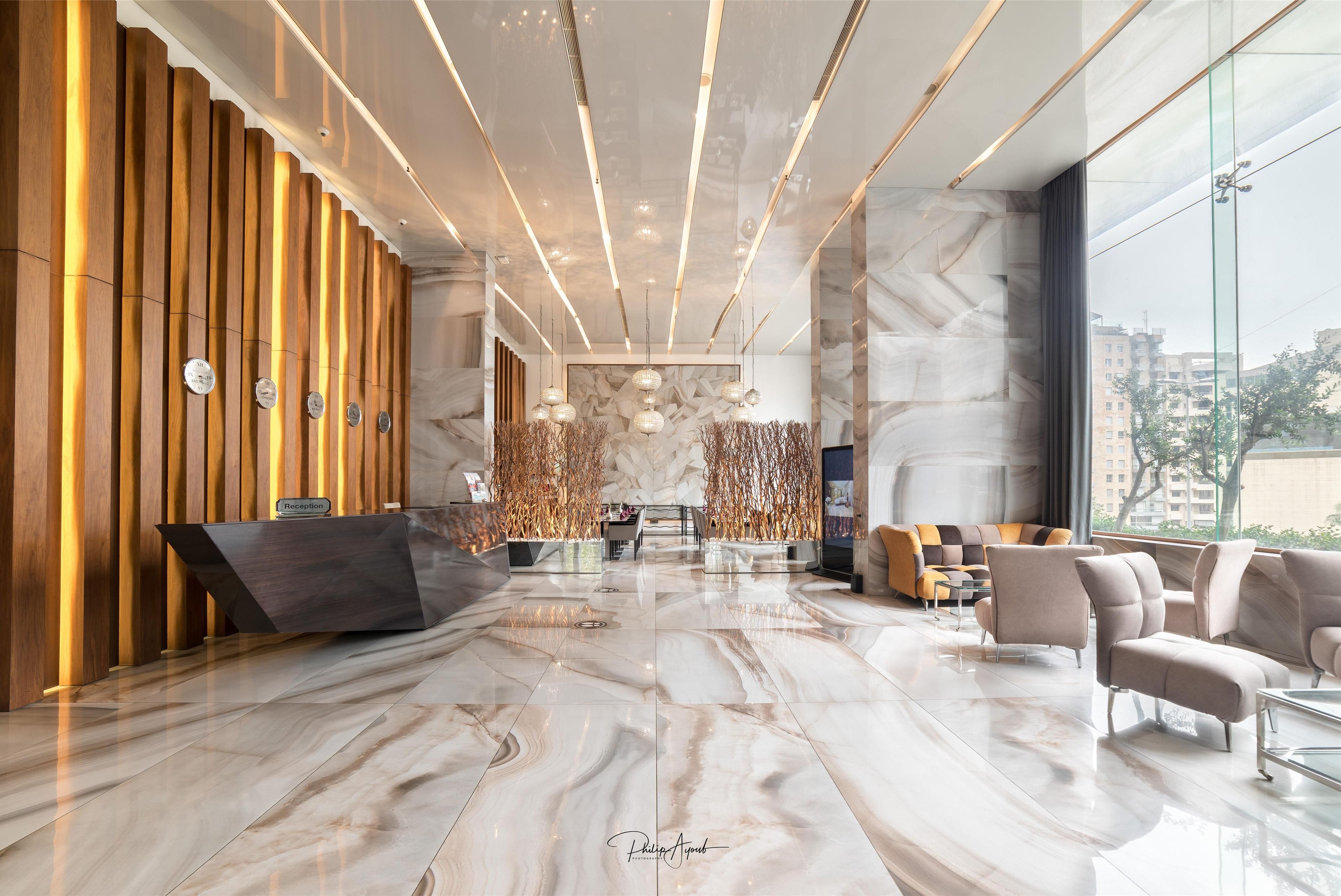 A modern lobby with a reception desk, seating area, and large windows offering views of the city.