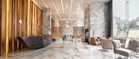 Un hall d’entrée moderne doté d’un comptoir de réception, d’un espace salon et de grandes fenêtres offrant une vue sur la ville.