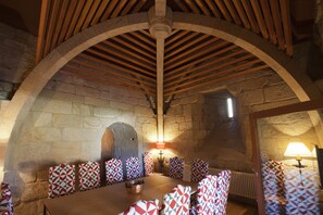 A dining area with a stone wall, wooden beams, and patterned chairs. - Parador Castillo De Monterrei (Monterrei)
