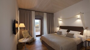 Een hotelkamer met een groot bed, een stoel, een klein tafeltje en uitzicht door een deur.