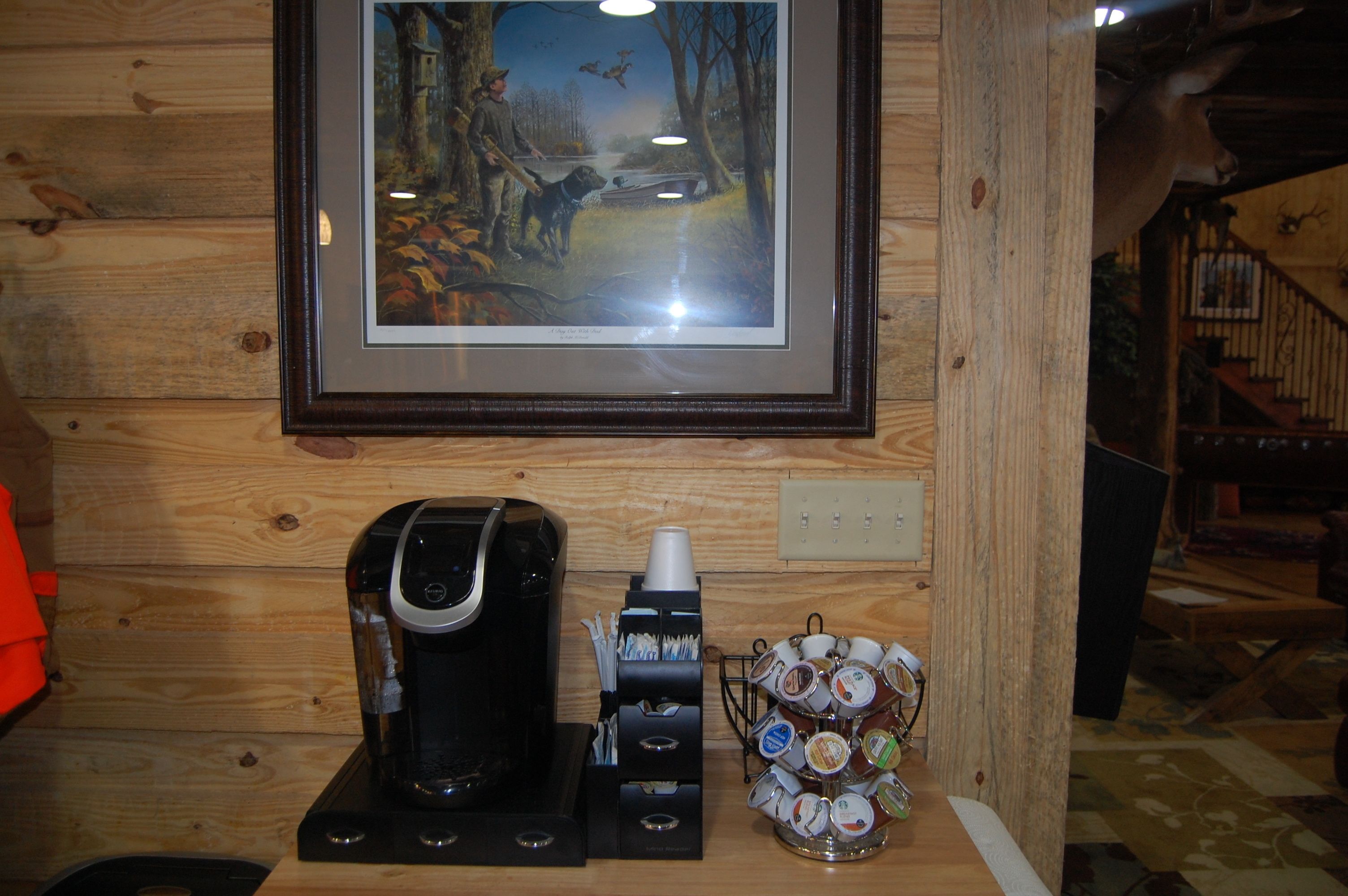 Ein gerahmtes Tiergemälde, eine Kaffeemaschine und ein Becherhalter mit Kaffeetassen auf einer Holzauslage.