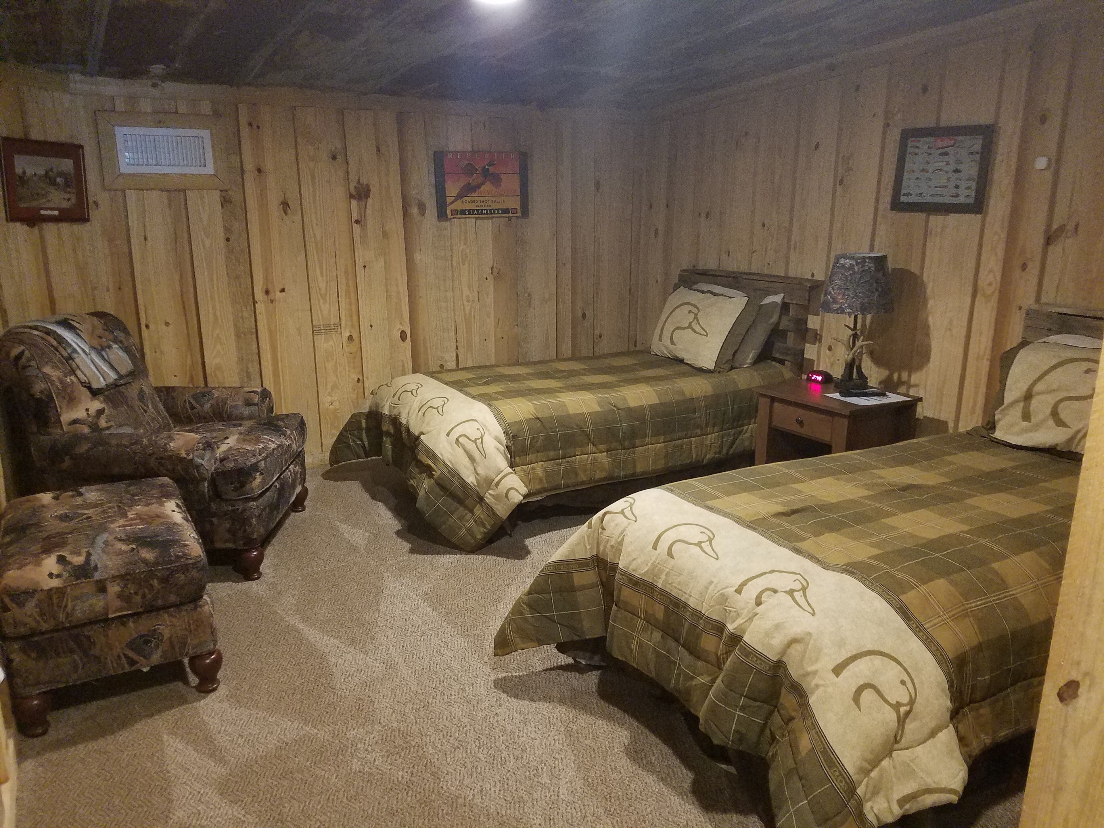 Ein Zimmer mit Holzboden, zwei Betten, einem Sessel und einem Nachttisch.