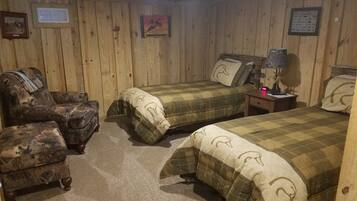 Ein Zimmer mit Holzboden, zwei Betten, einem Sessel und einem Nachttisch.