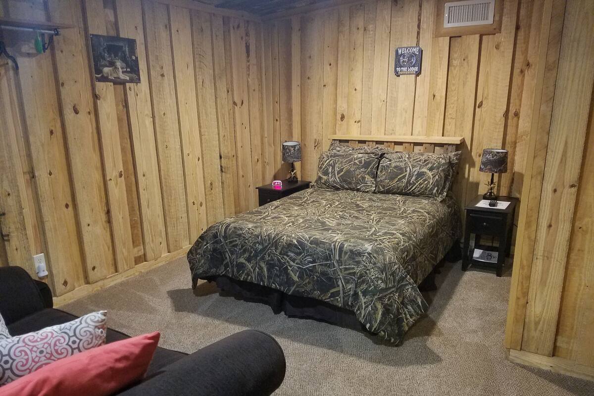 Ein Zimmer mit Holzwandverkleidung, einem Bett, einem Nachttisch, einer Lampe und einem Schild mit der Aufschrift 'Welcome to the Lodge'.