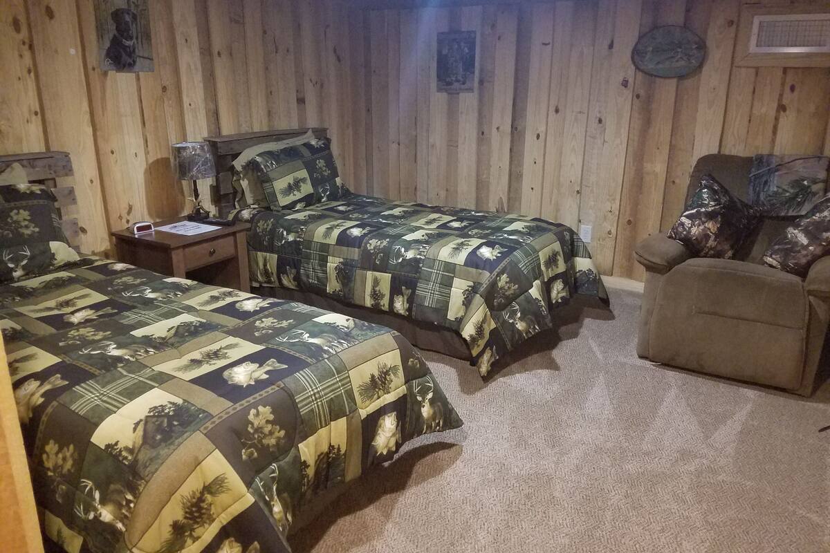 Ein Zimmer aus Holz mit zwei Betten, einem Sessel und einem Nachttisch.