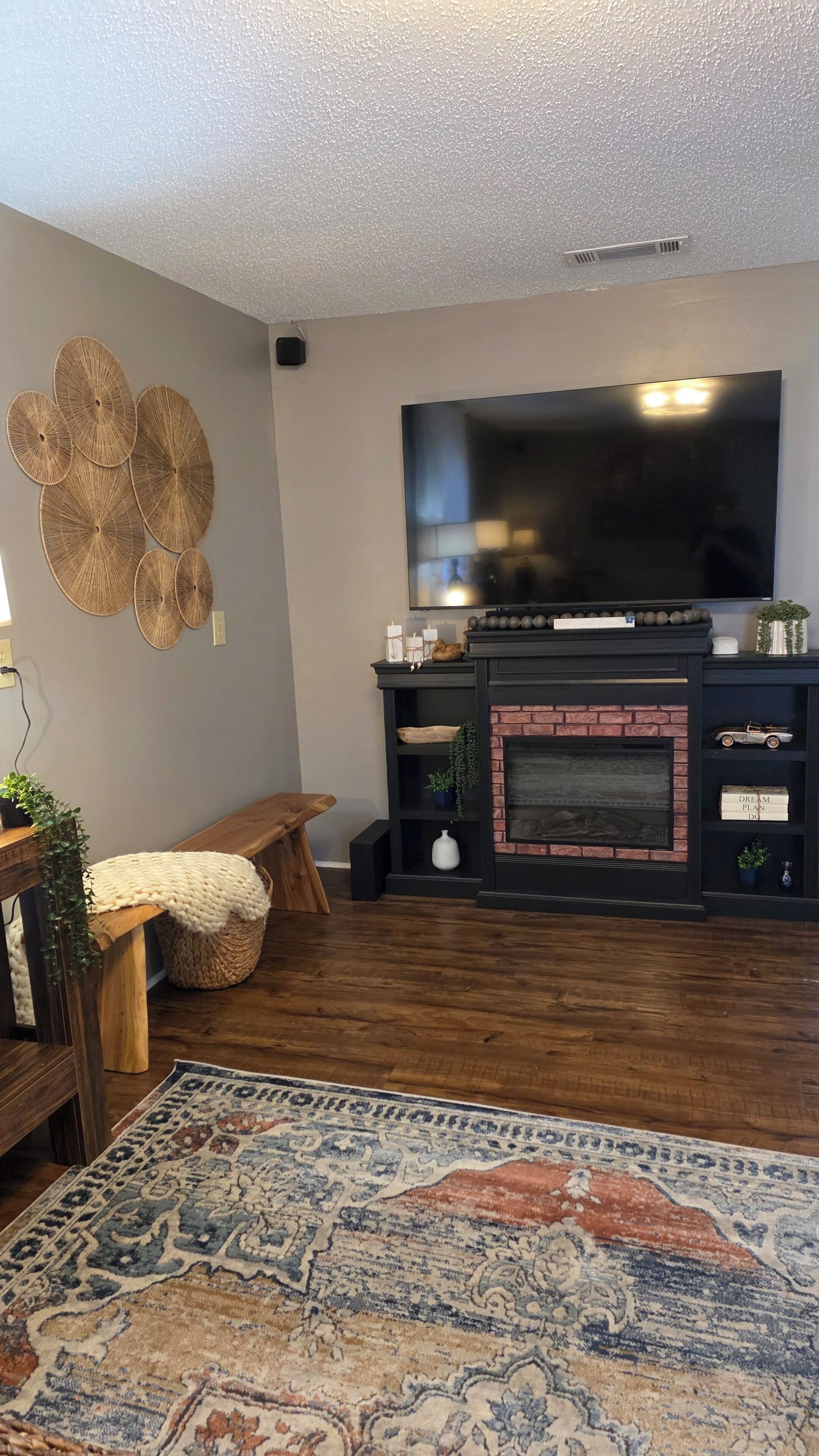 A living room with a fireplace, a television mounted on the wall, and a patterned rug on the floor.