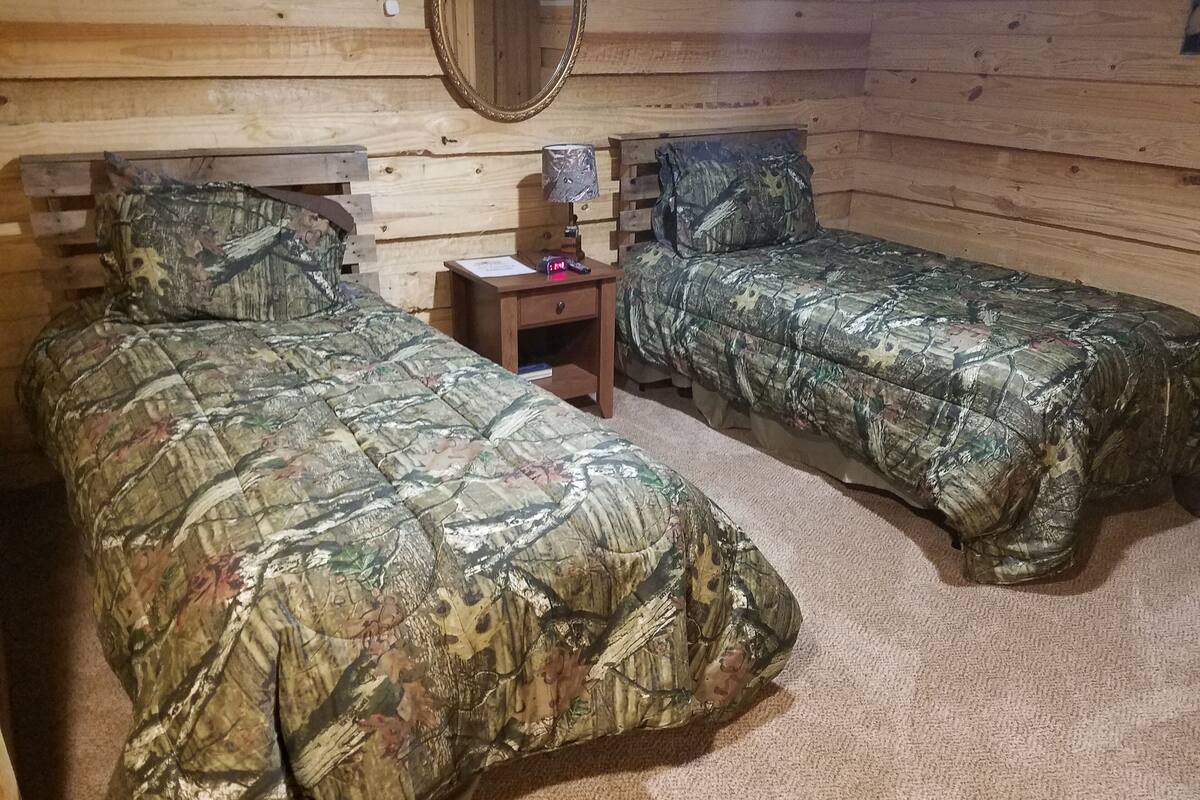 Ein Holzhütten-Zimmer mit zwei Betten, einem Nachttisch, einer Lampe und einem Spiegel.
