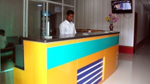 A reception desk with a clock above it, a TV mounted on the wall, and a vase with flowers on the counter. - Aung Tha Pyay Hotel 2 (Yangon)