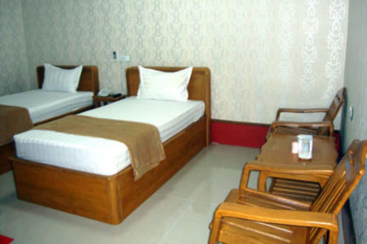 A room with two single beds, a wooden table with chairs, and a small table with a glass.