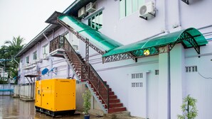 A building with a staircase leading to a balcony, a yellow utility box, and potted plants. - Aung Tha Pyay Hotel 2 (Yangon)