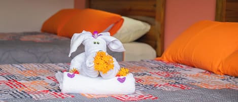 Un lit avec une couvre-lit à motifs, une serviette décorative ornée d’un motif de lapin, et deux coussins orange.