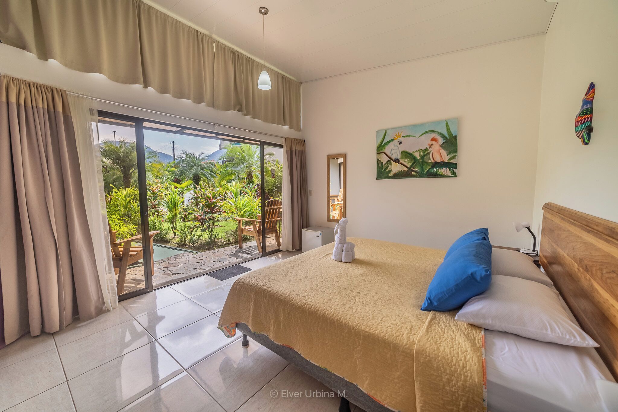 A bedroom with a bed, a view of a garden through a sliding door, and a painting on the wall.