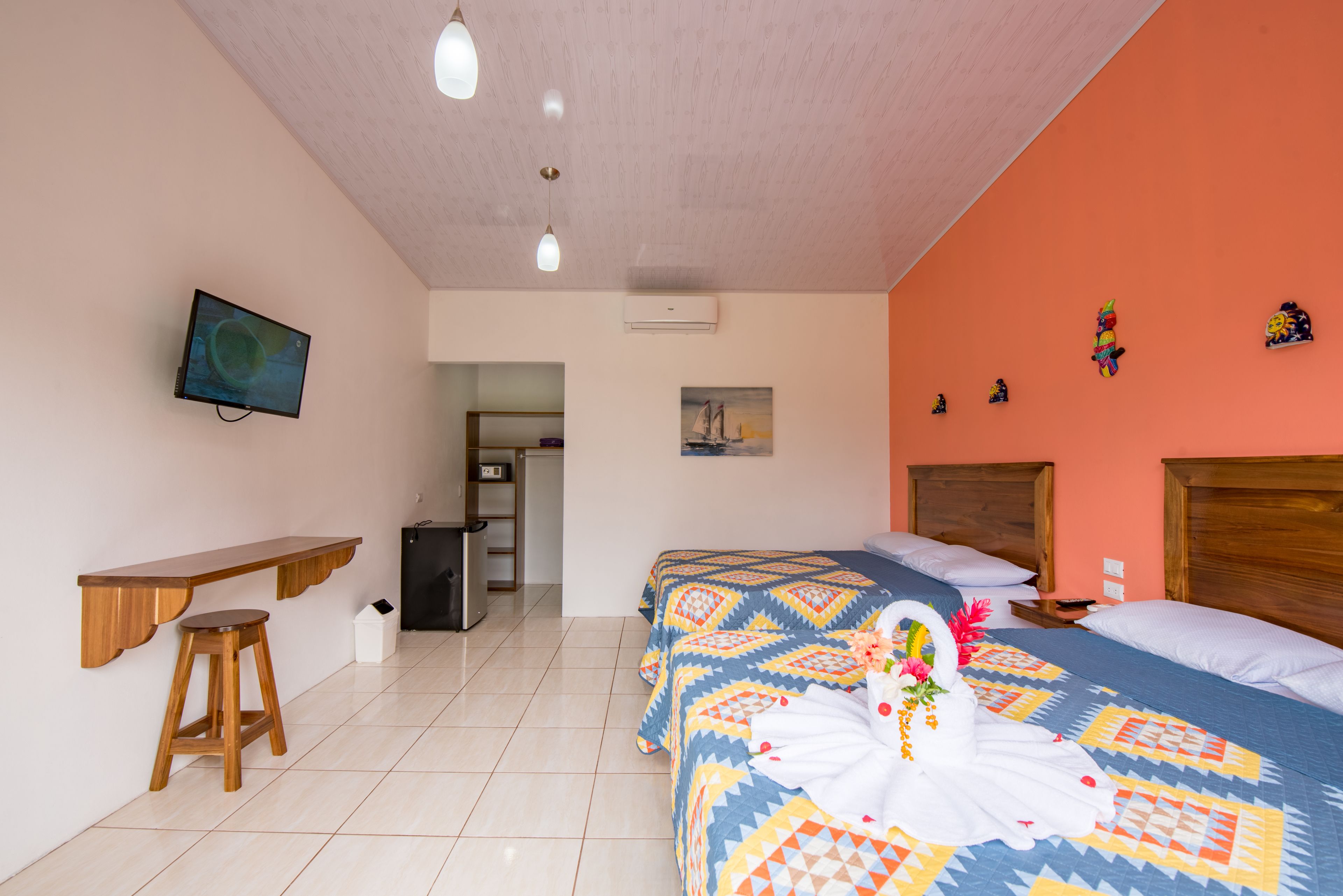 Habitación de hotel con dos camas, televisión, estante de madera, taburete y una pequeña kitchenette.