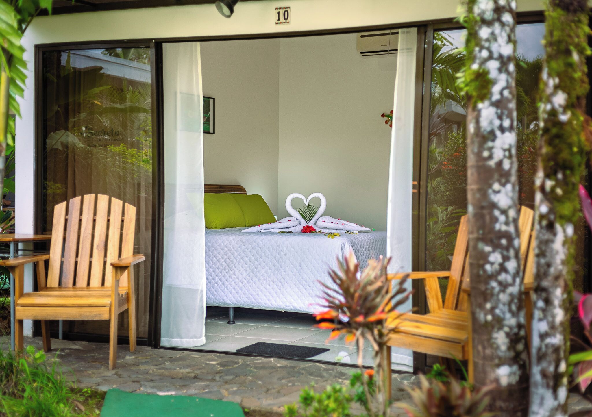 Una habitación con una cama, dos sillas de madera y un ventanal de vidrio que da a un jardín.